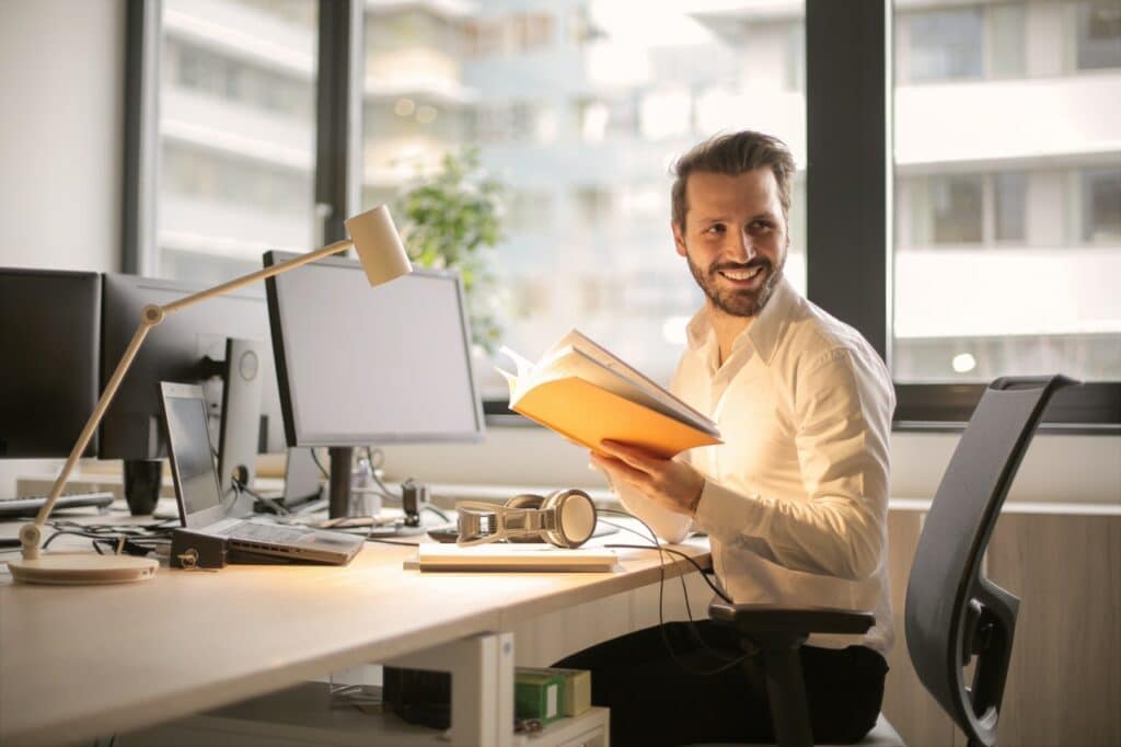 Man holding book in front of multiple monitors