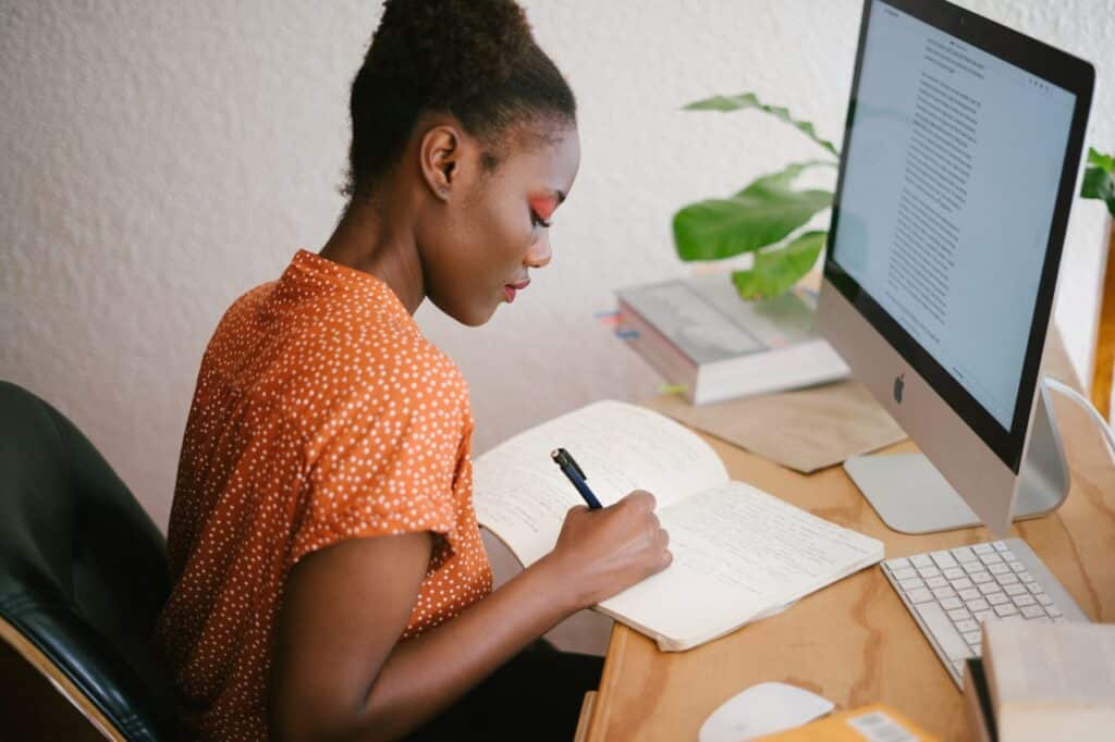 Black woman in front of her computer to help write faster and wondering is blogging worth it and how to turn blogging into a career