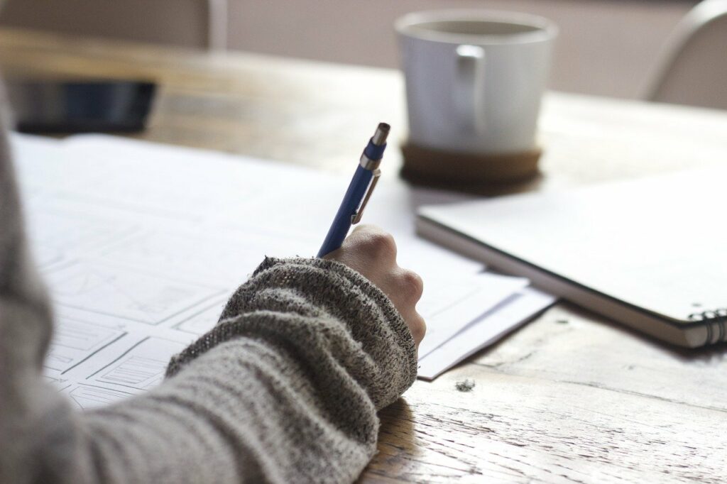 Blogger writing at a desk with coffee. Keep. reading to know how to write blog posts faster.