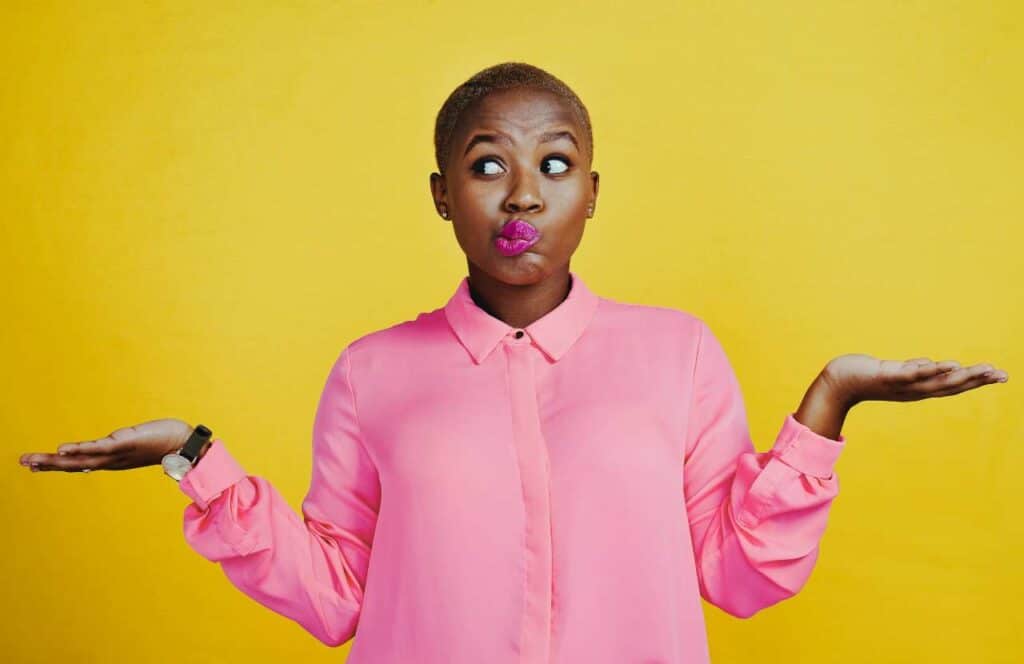 A black woman with pink lipstick and pink shirt standing with her palms facing up as if she is confused. Learn more about conversion rate optimization for your blog.
