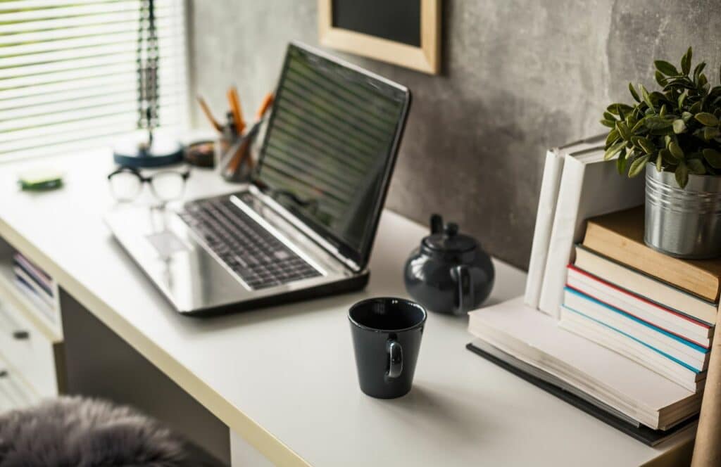A clear workspace at desk with a tea kettle, cup, and stack of books. Keep reading for tips on how to write blog posts faster.