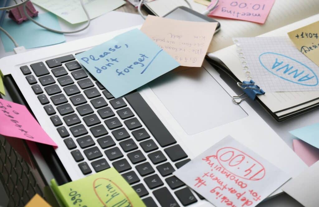 A messy and overwhelming workspace at desk with lots of sticky notes. Keep reading for tips on how to write blog posts faster.