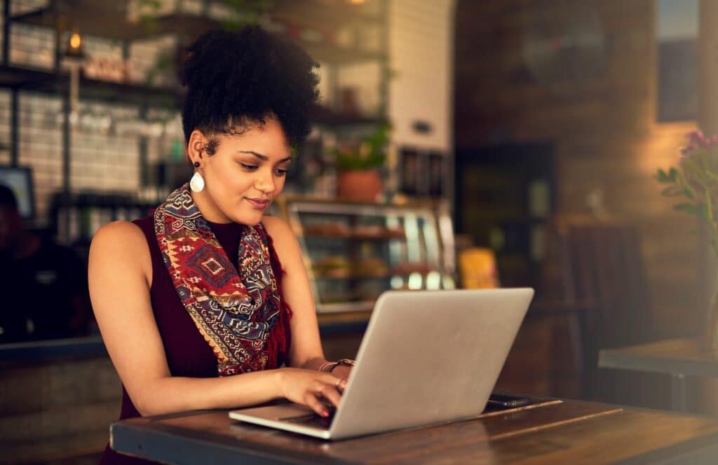 A woman sitting at a wooden table editing a blog post. Keep reading for tips on how to write blog posts faster.