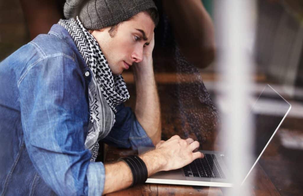 Man sitting in coffee shop with a blank screen due to writers block. Keep reading for tips on how to write blog posts faster.