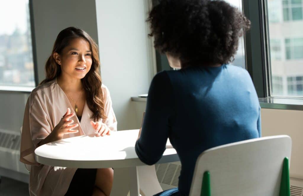 Two women talking can inspire a conversational tone with blog writing. Keep reading for tips on how to write blog posts faster.