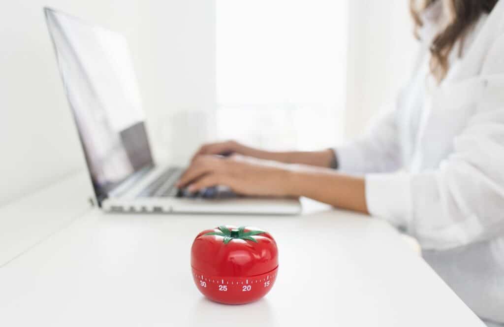 Woman typing at clean desk with a pomodoro timer for productivity. Keep reading to know how to write blog posts faster.