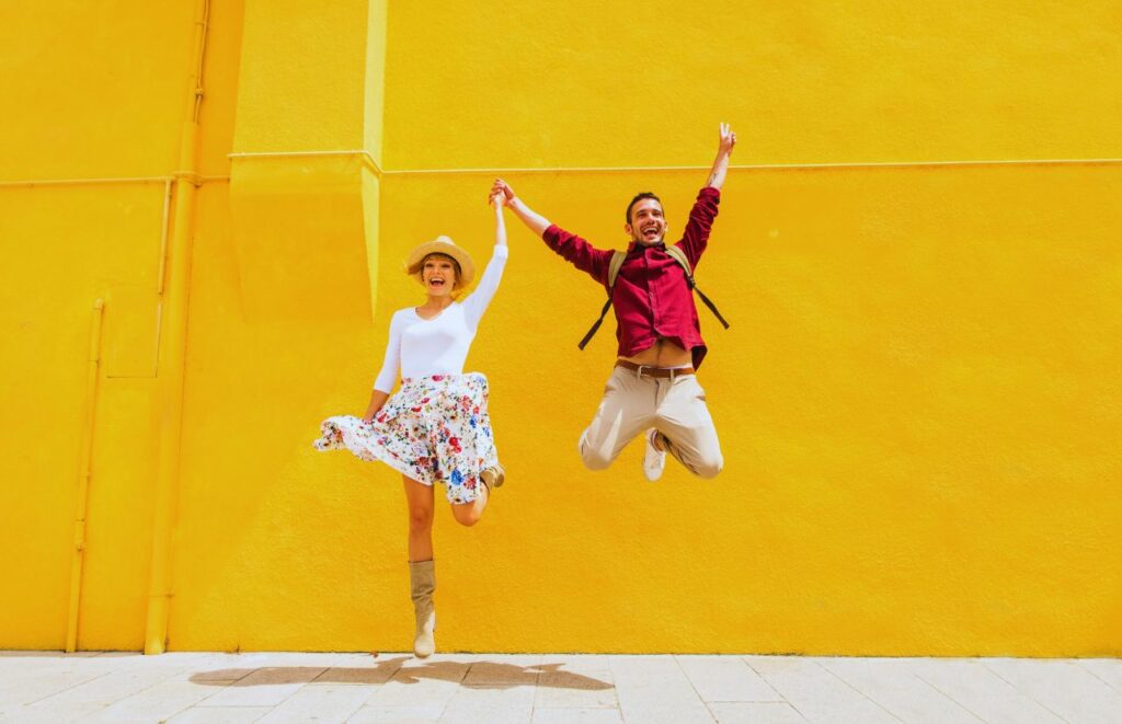 Blog Writers Jumping up and down against yellow wall. Keep reading to learn where to find blog writers and quality freelance content writers for your blog.