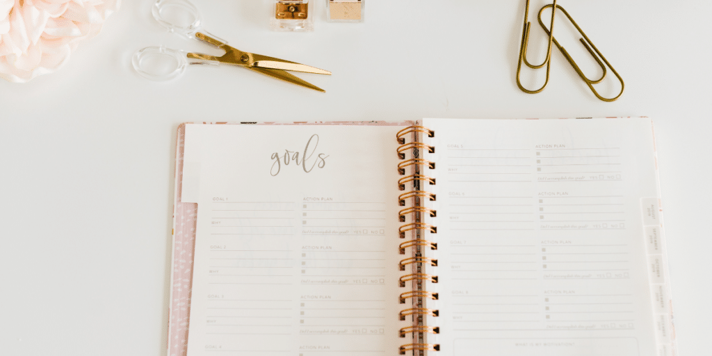 desk with scissors, paperclips, and an agenda open to a page that says Goals