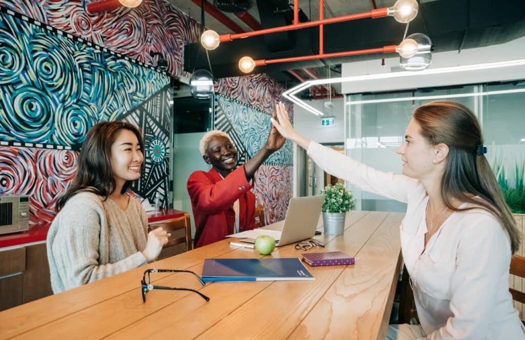 Bloggers and Freelance ladies giving a high five at the the table. Keep reading to know How Much to Charge for a Blog Post