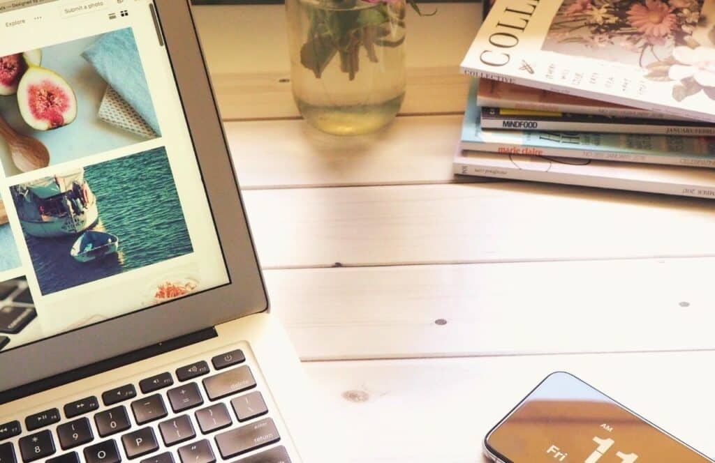 Laptop on the table next to phone and magazines. Keep reading to know How Much to Charge for a Blog Post