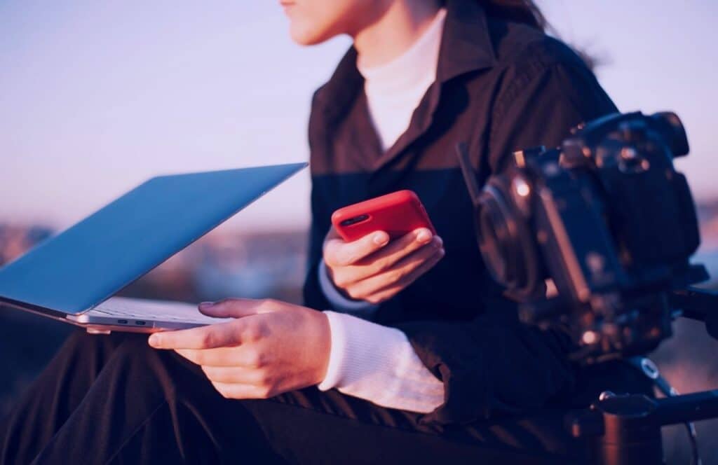 Woman blogger outside with computer and camera thinking about what to charge for an article. Keep reading to know How Much to Charge for a Blog Post