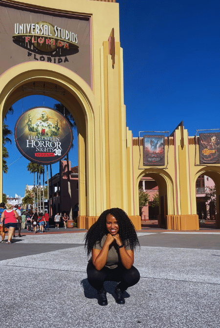 NikkyJ of ThemeParkHipster in front of the Universal Studios Florida Entrance Arches Solo Travel Guide. Keep reading to learn how this theme park blogger and Disney blogger makes money.