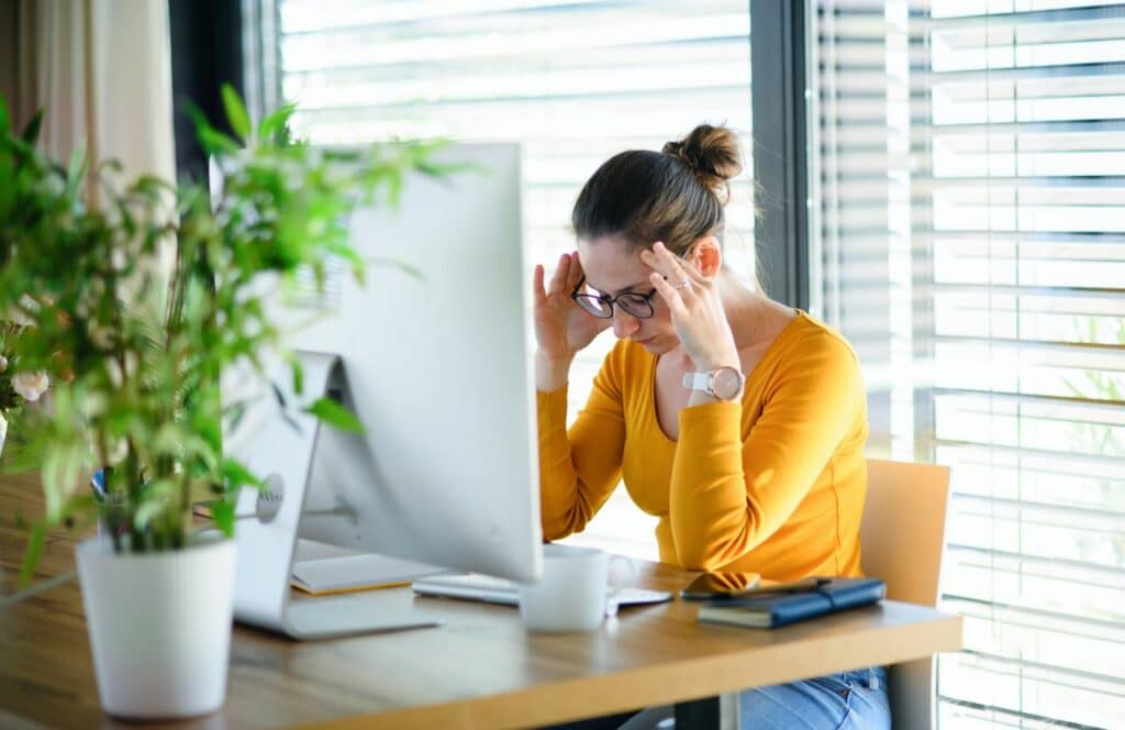 A-woman-stressed-with-her-head-down-at-her-desk-with-computer.-Keep-reading-for-tips-on-how-to-write-blog-posts-faster