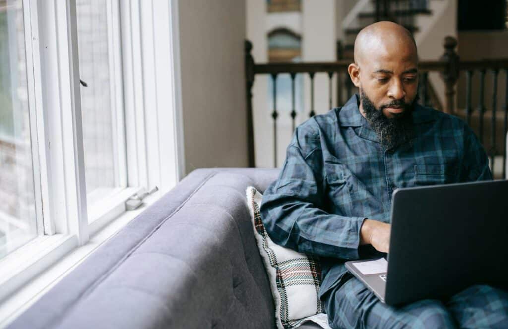 A black man sitting by a window and working on his freelance business and blog. Read more to learn how to do a technical site audit after the Google update.