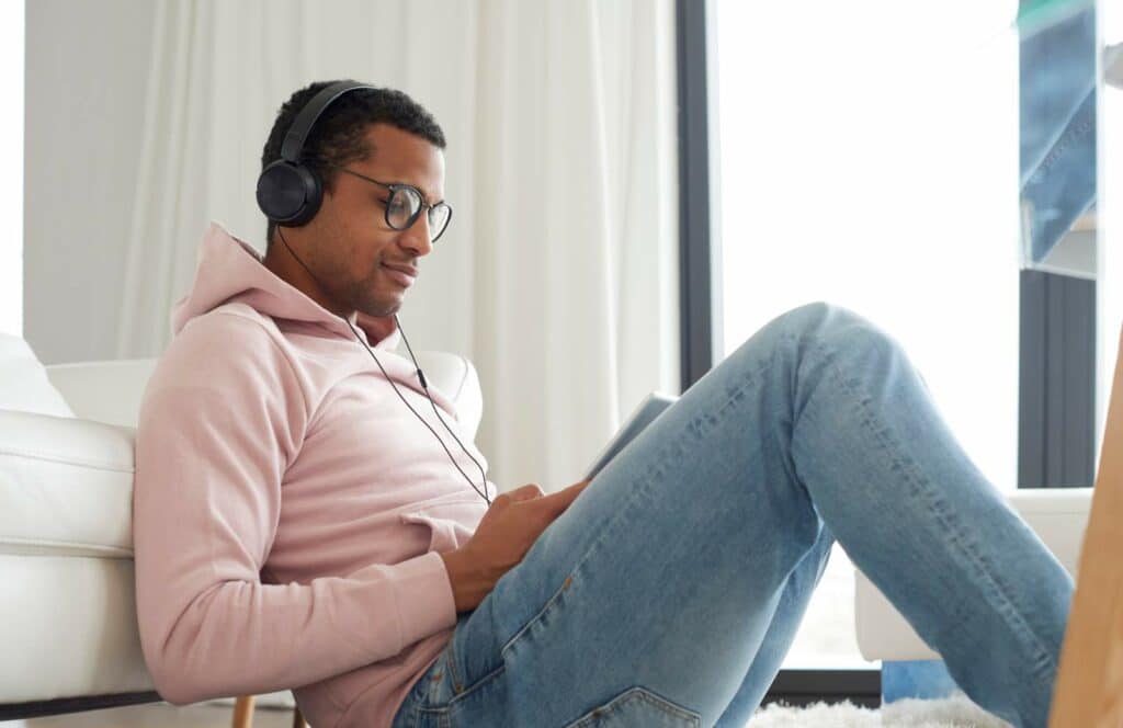 A man sitting on the floor while on his laptop meeting with a coaching client as a result of marketing his services on his blog. Keep reading to learn how to monetize your blog from day one.