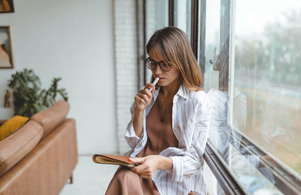 A woman sitting next to a large window as she thinks about starting a podcast. Read more to learn how to monetize your blog from day one.