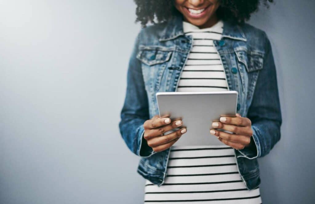 A black woman with curly hair standing agains a grey wall while reading a recently published blog post. If you have ever asked "What's the point of blogging?" click here to read more.