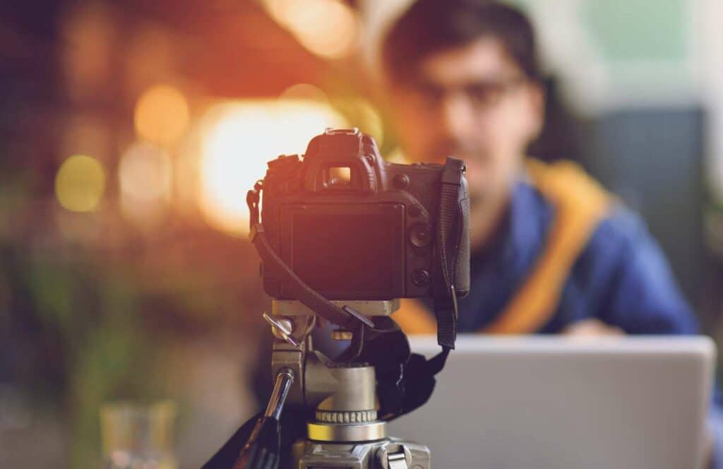 A camera pointing at a man sitting at his laptop while creating content for a blog. If you have ever asked "What's the point of blogging?" click here to read more.