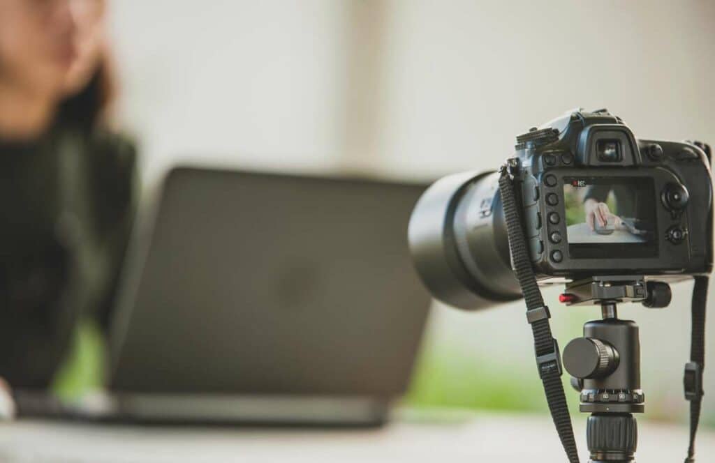 A camera pointing at a woman sitting at her laptop while creating content for her blog. If you have ever asked "What's the point of blogging?" click here to read more.