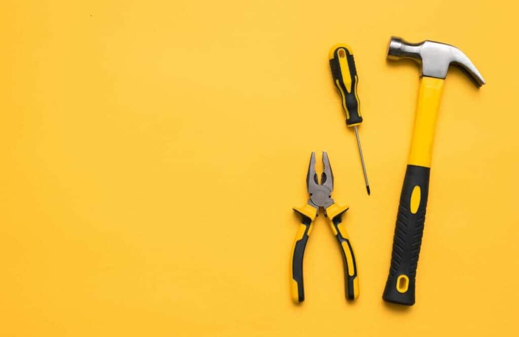 A hammer, screwdriver, and pliers laying on a yellow background signifying how bloggers needs tools to better optimize their blogging business. Learn more about conversion rate optimization for your blog.