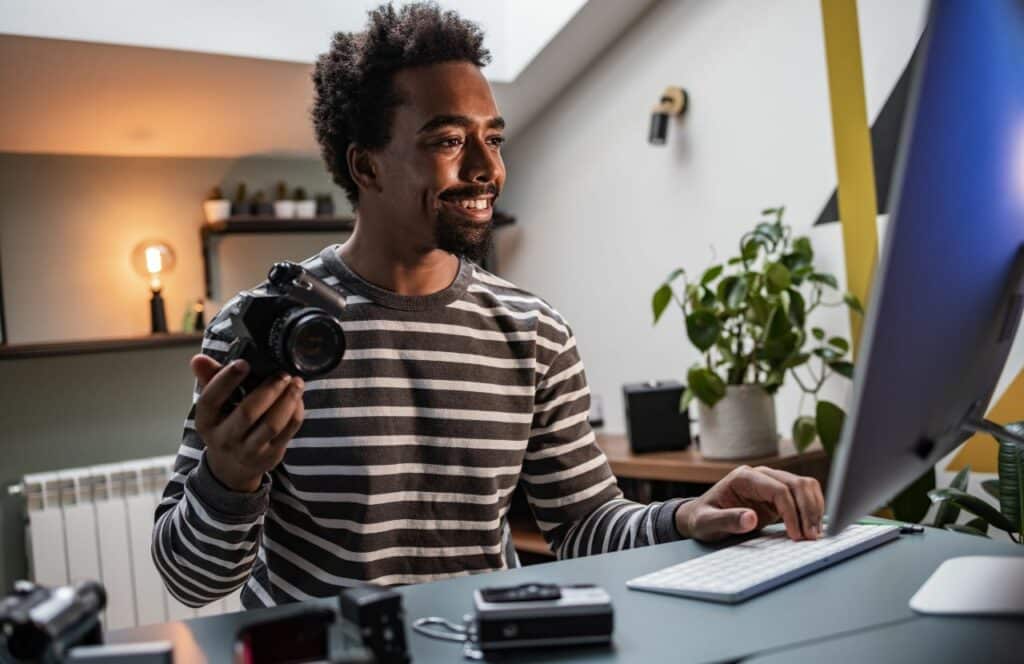 A man holding a camera in one hand while typing with the other hand to download images for his blog. If you have ever asked "What's the point of blogging?" click here to read more.