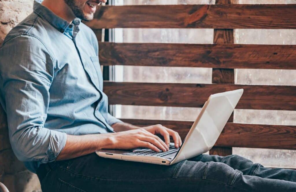 A man sitting against a stone wall while writing his next blog post for his readers. If you have ever asked "What's the point of blogging?" click here to read more.