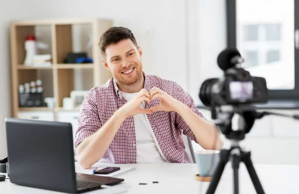 A man sitting in front of a camera and laptop while forming a heart with their hands to communicate their appreciation for their blog audience. If you have ever asked, "What's the point of blogging?" keep reading because content is king.