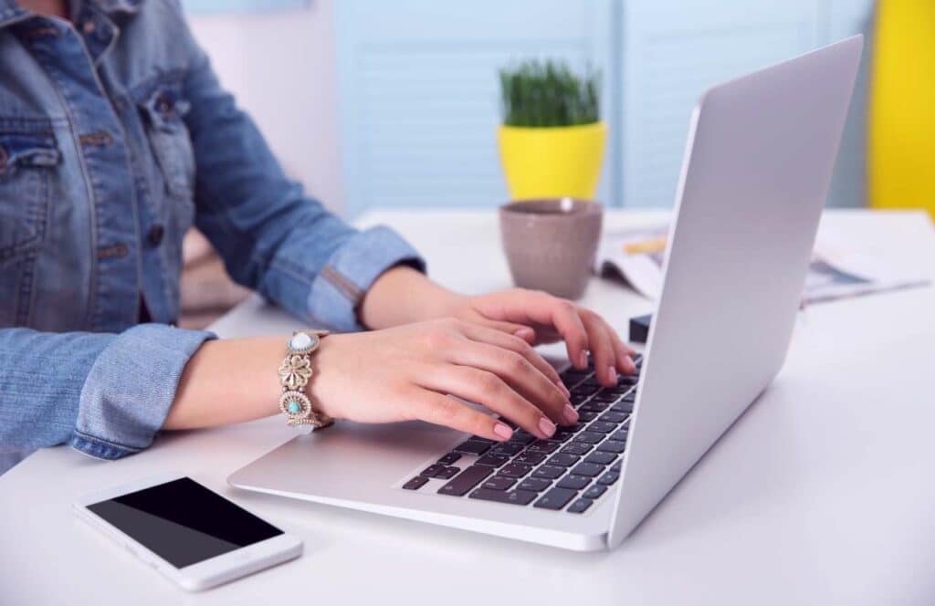 A woman in a blue jean jacket typing on her laptop while finishing up her long-form content. If you have asked "What's the point of blogging?" click here to read more.