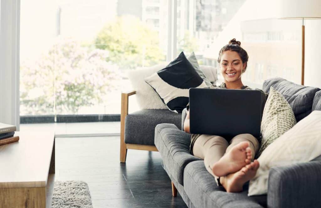 A woman sitting comfortably on her couch while writing a blog post in front of an open window. If you have ever asked "What's the point of blogging?" click here to read more.