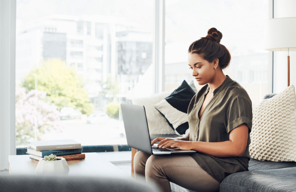 A woman sitting on the couch working on her blog with the goal of becoming a full-time blogger. Keep reading to learn the answer to the question, "Is Blogging Still Relevant?"