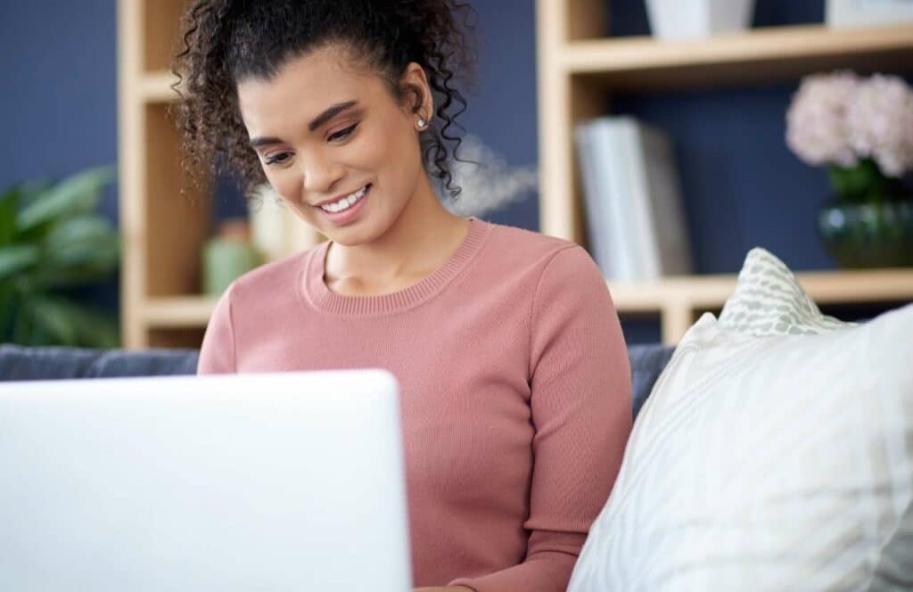 A woman with curly hair sitting in a blue room while working on her next blog post. If you have ever asked "What's the point of blogging?" click here to read more and learn how to write a blog post in 30 minutes.