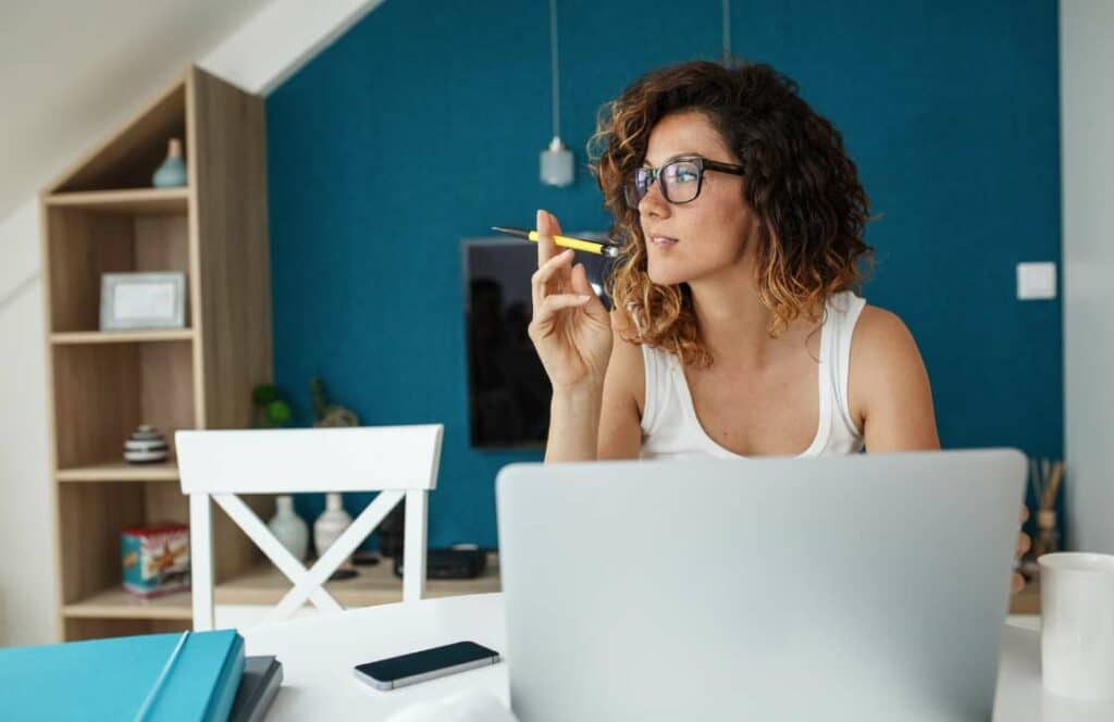 A woman with shoulder length wavy hair sitting in front of her laptop and thinking of creative blog post ideas. If you ever wondered "What's the point of blogging?" click here to read more.