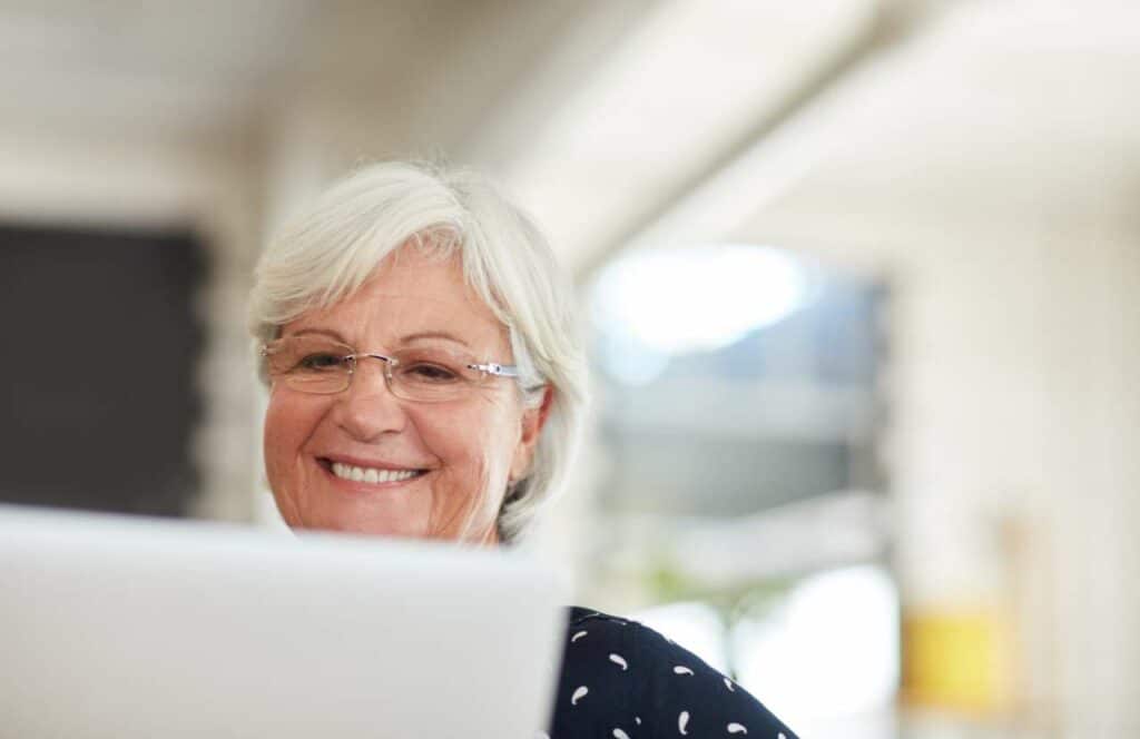 An older woman smiling and working on creating valuable content for her blog. If you have ever asked The letters of the word _blog_ in all caps with each letter on a wooden block in a share of blue or purple. If you have ever asked "What's the point of blogging?" click here to read more.
