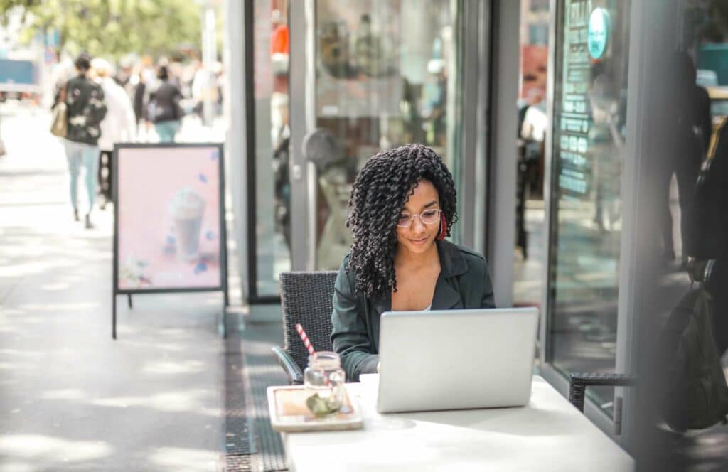 A black woman sitting at a table outside of a coffee shop while working on her blog linking strategy. Learn more about internal linking best practices by reading this blog post.