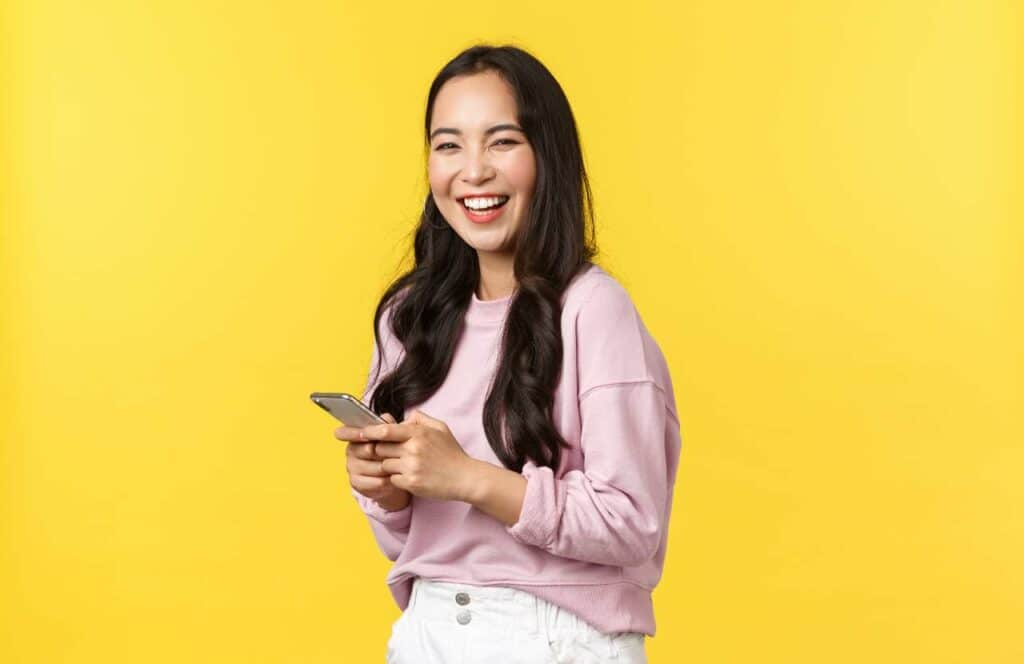 A smiling woman standing in front of a yellow background with her phone as she reads tips about blog brand awareness