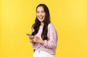 A smiling woman standing in front of a yellow background with her phone as she reads tips about blog brand awareness