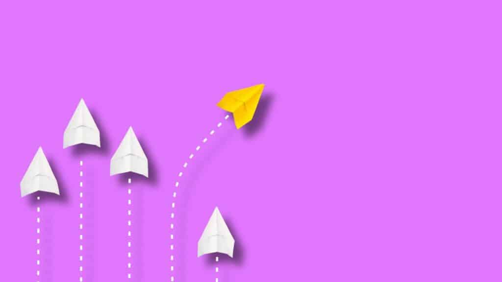 A group of paper airplanes soaring through the air against a purple background. Click here to learn more about affiliate vs partner marketing for bloggers.