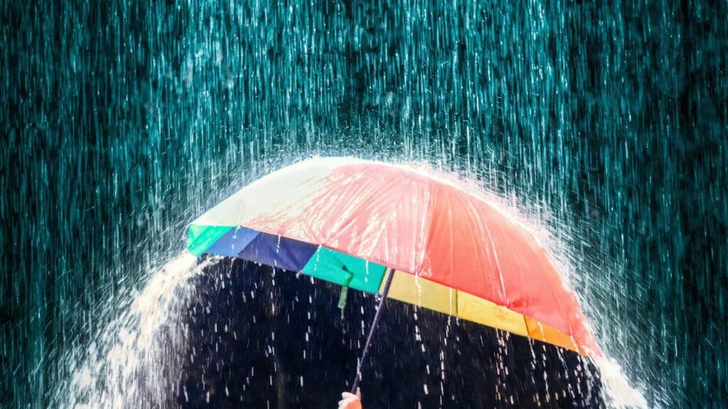 A person holding an umbrella in the rain, seeking shelter from the downpour. Click here to learn more about affiliate vs partner marketing for bloggers.