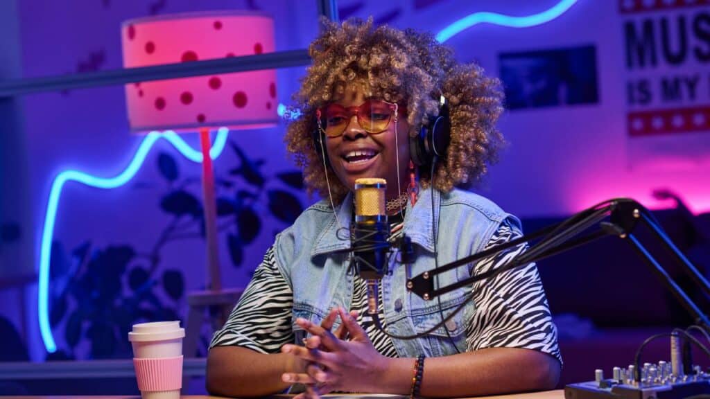 A woman with curly hair wearing headphones, sitting at a table.