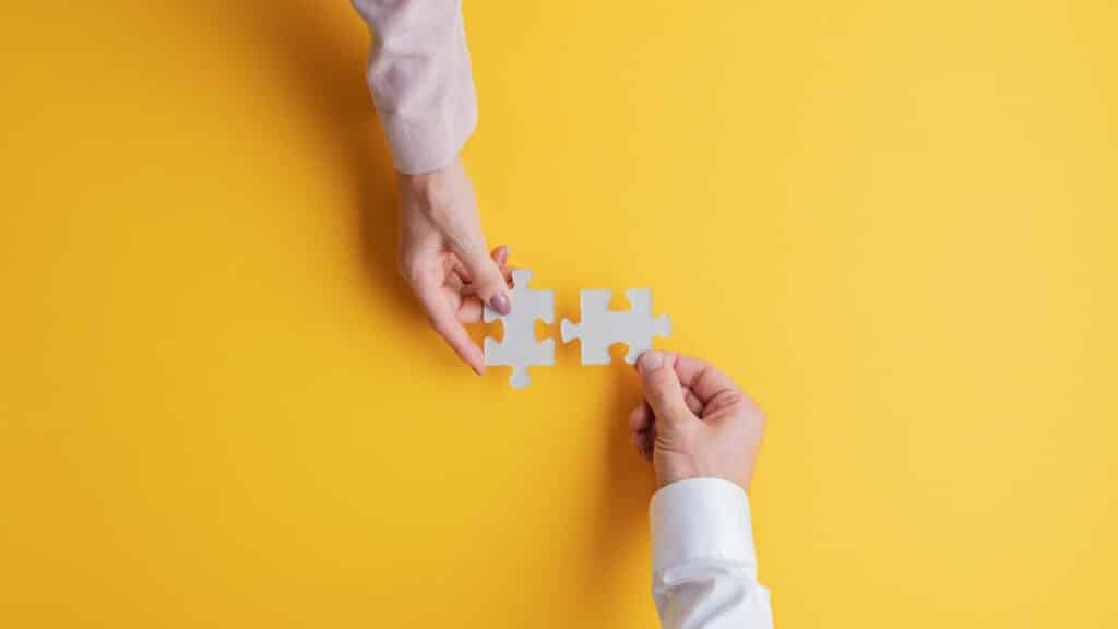 Two people holding a puzzle piece on a yellow background