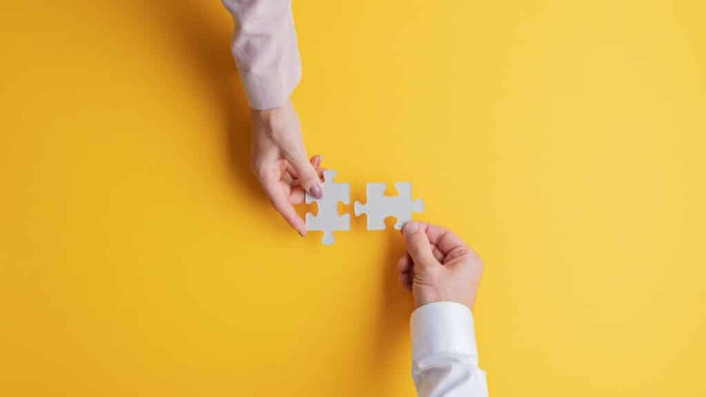 Two people holding a puzzle piece on a yellow background
