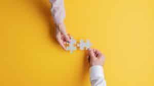 Two people holding a puzzle piece on a yellow background